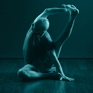 Man in a sitted yoga pose with one leg stretched upward and a hand holdiing the foot