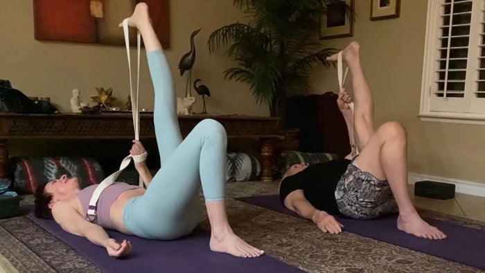 A man and woman doing yoga at home, lying on the floor with resistance bands