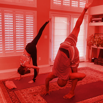A man and woman doing yoga with one leg raised upward and head down